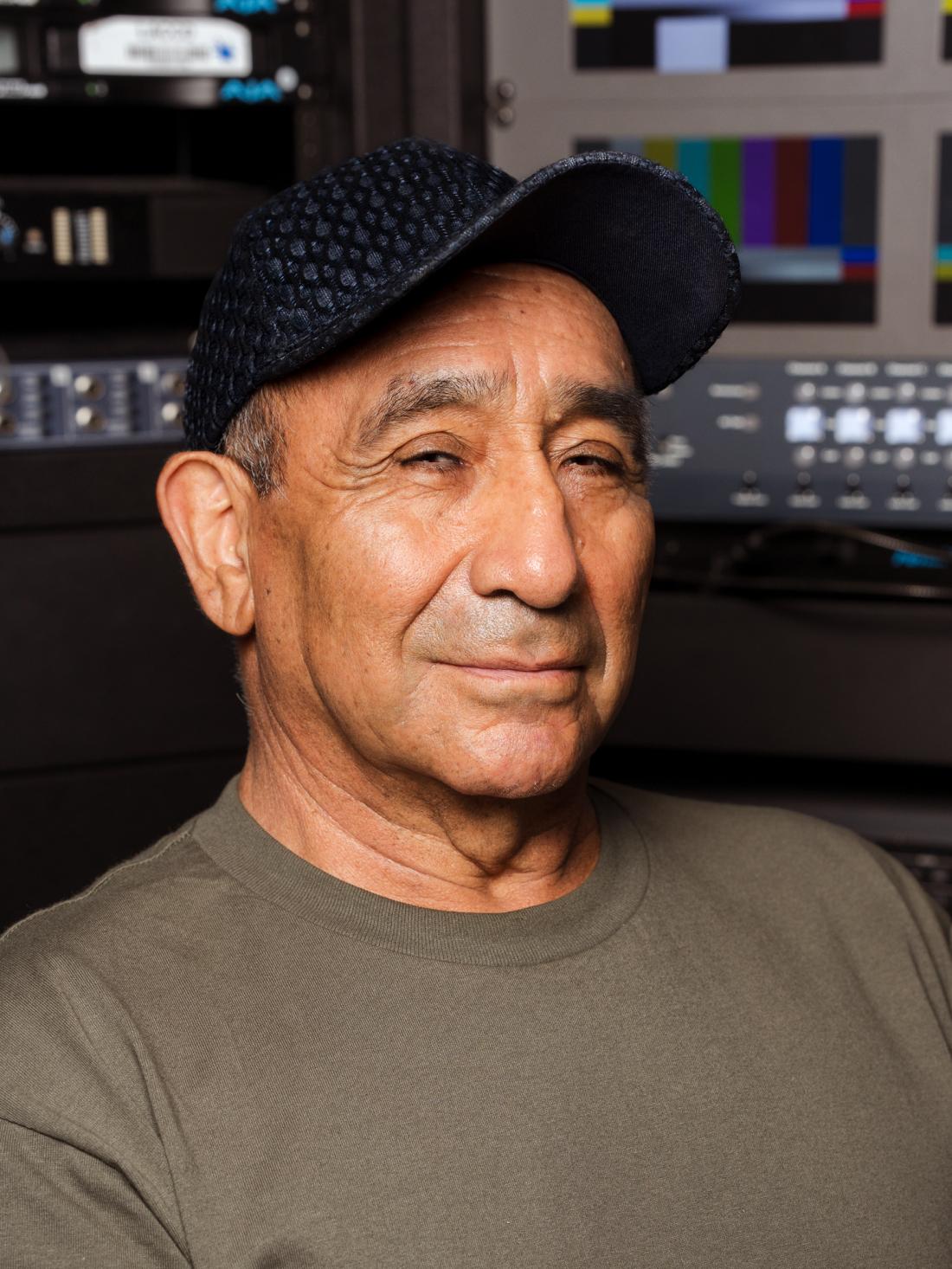 Headshot of LACC Cinema & TV Video Engineer Juan Kalafatovich against a live video playback bay