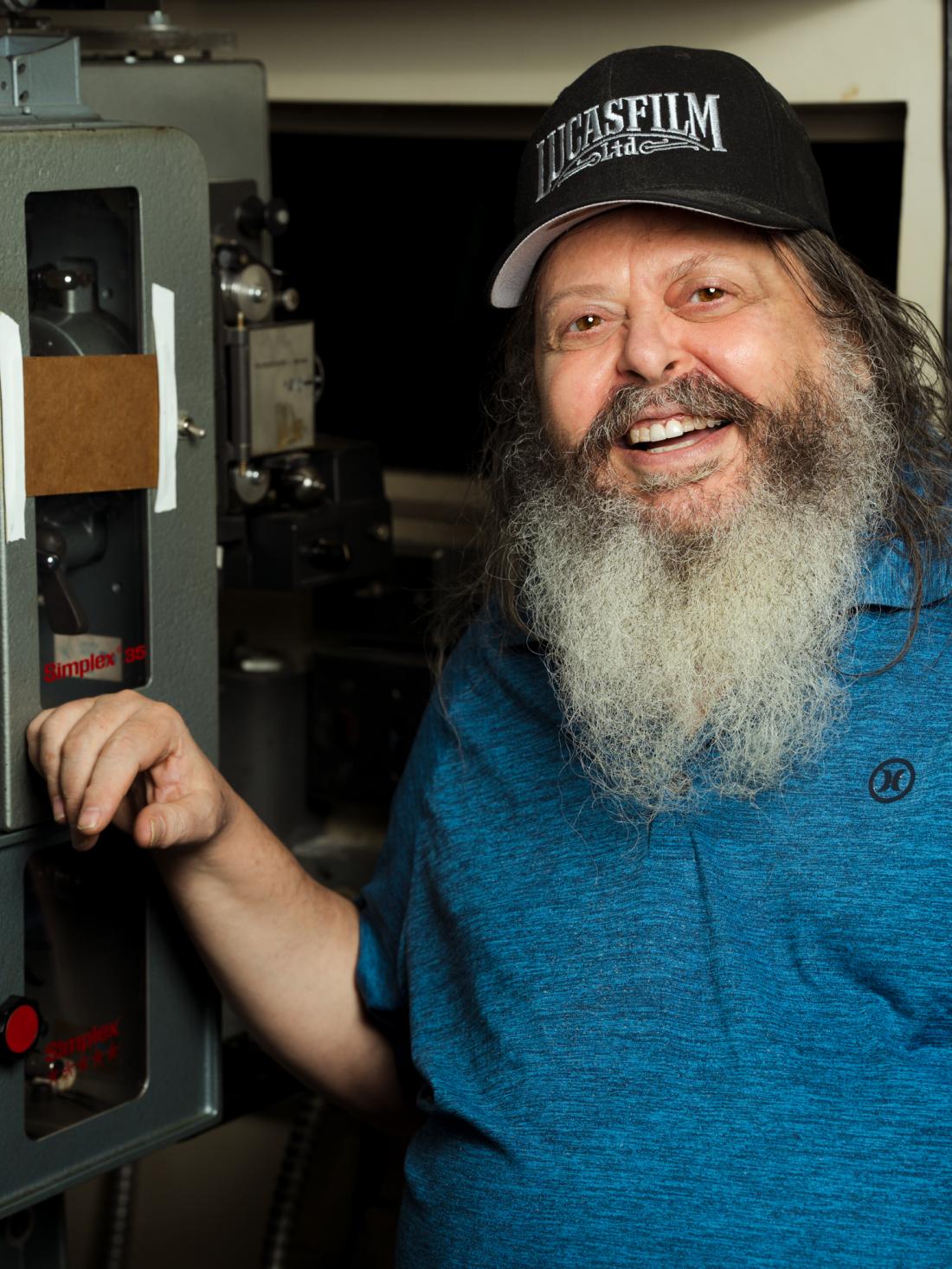 Amos Rothbaum, LACC Projectionist, posing next to Christie 35mm film projector.